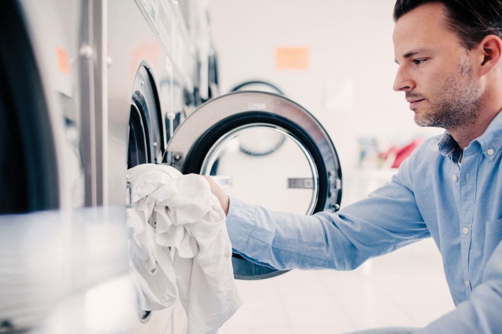 man putting clothes into washing machine