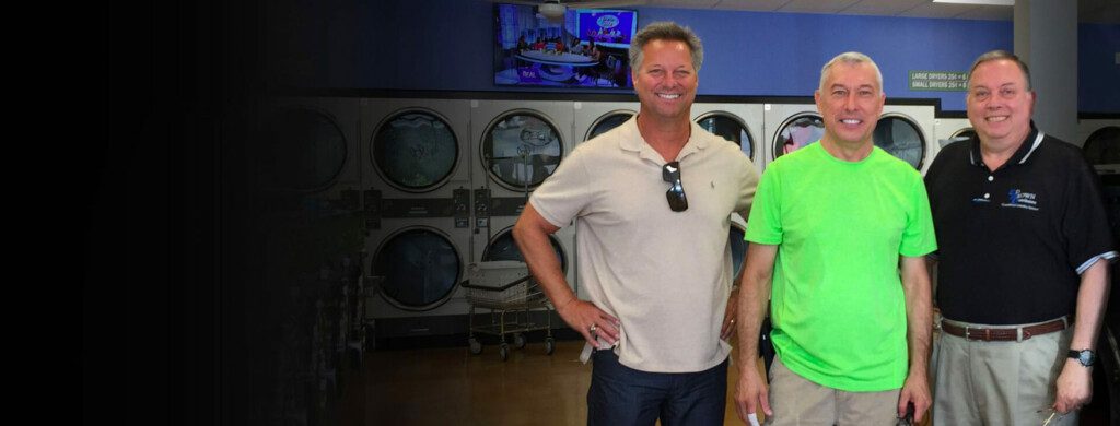 3 men standing in laundromat, smiling