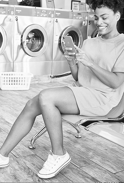 SectionC-BKGD woman smiling and looking at her phone in a laundromat