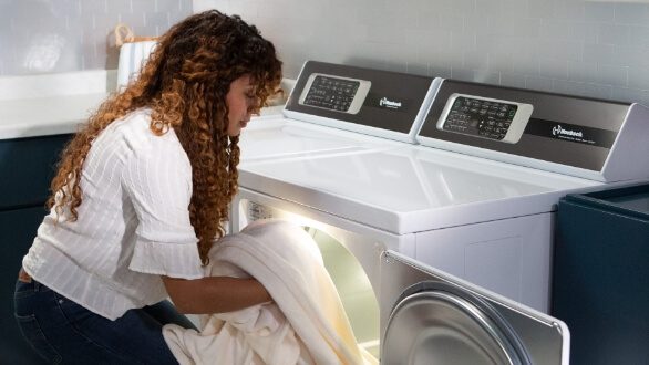 young woman putting bedding into dryer